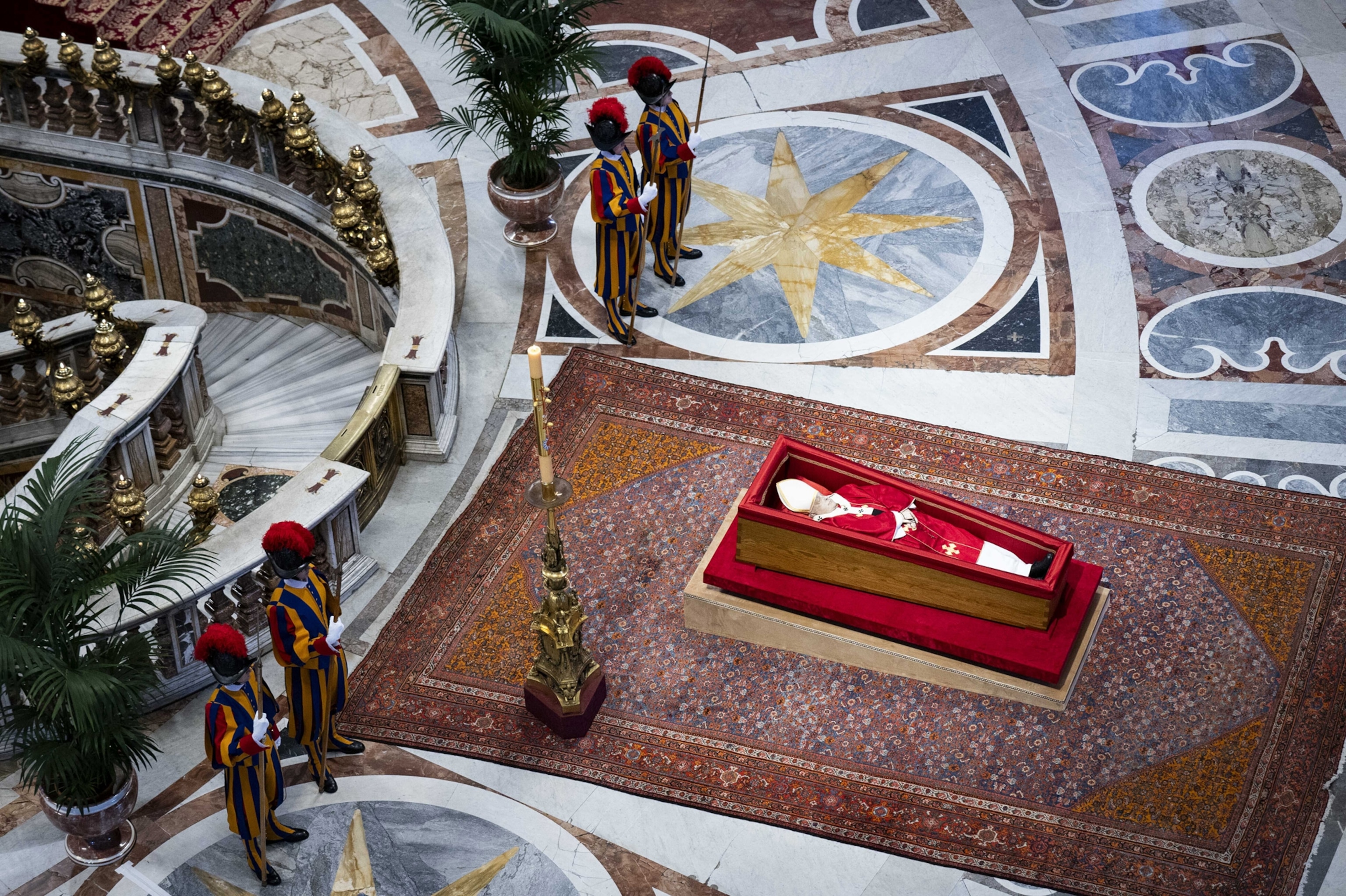 A aerial view shows the deceased Pope Francis lying in a wooden casket inside of a basilica.