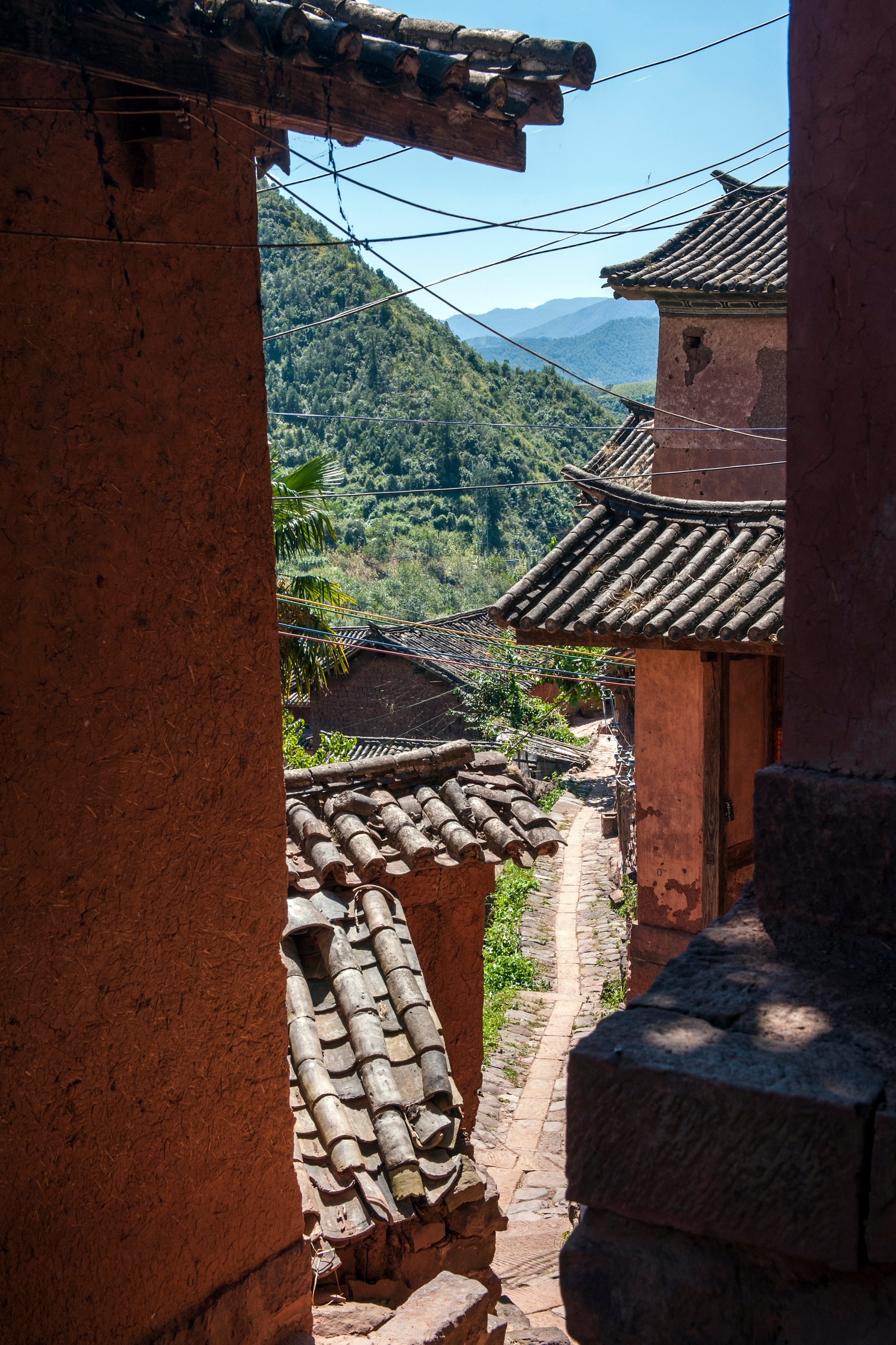 A trail seen through tan houses, lush green mountains sit in the background.