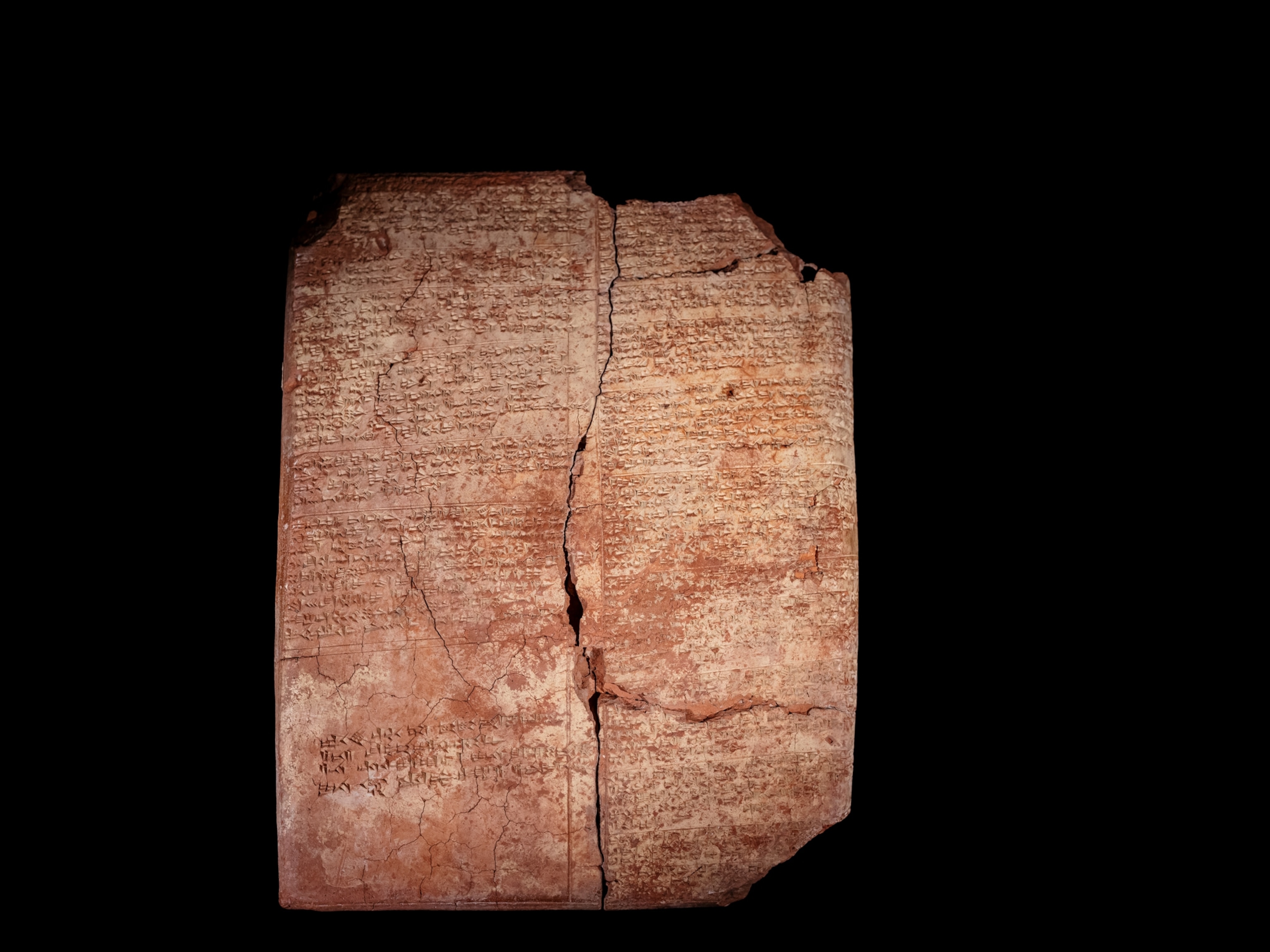 A clay tablet with a large crack going all the way down the center. The tablet has inscriptions of two languages.