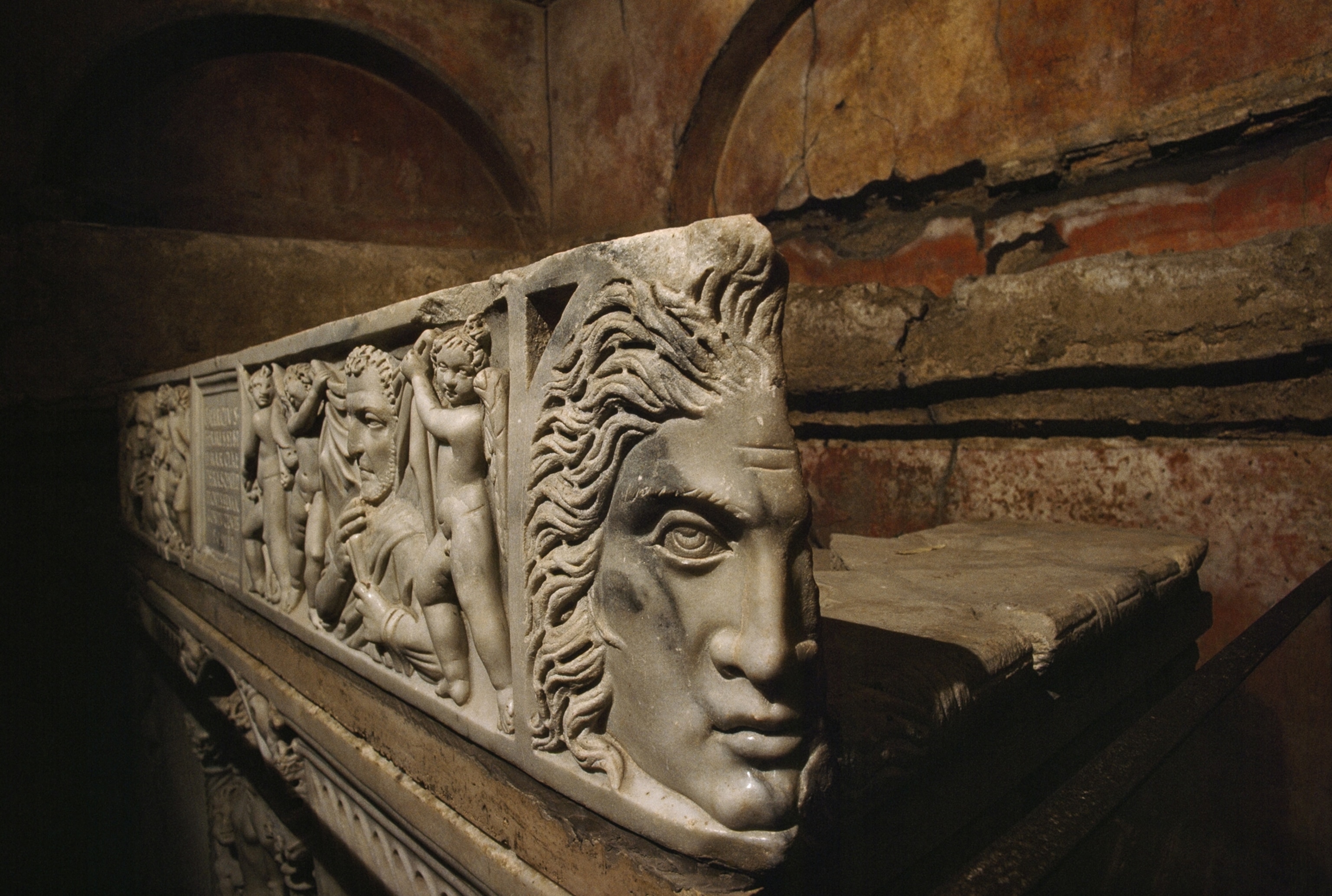 A close-up image shows engravings of faces in the structure of a marble sarcophagus.